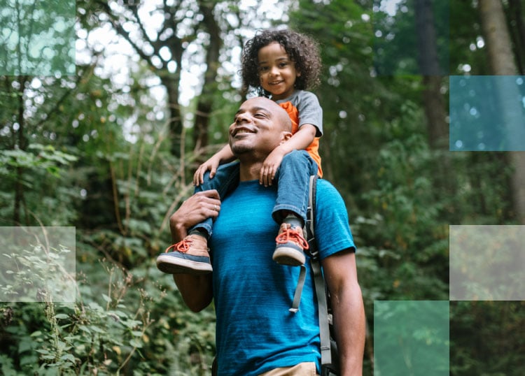 Father with child on his shoulders in a lush green forest on a hike.